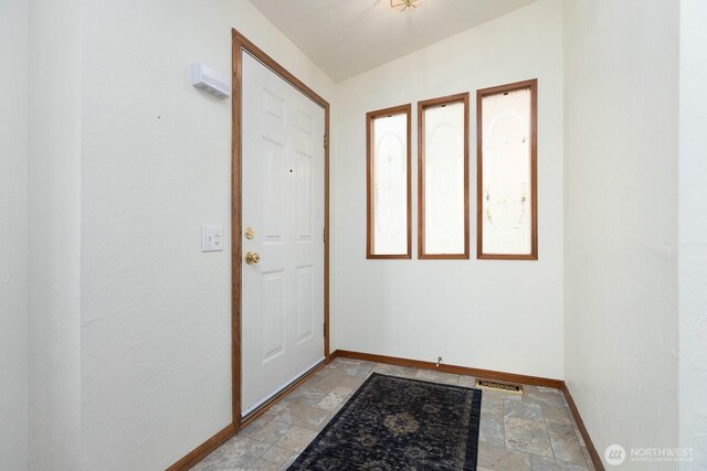 doorway to outside featuring baseboards, stone tile flooring, and visible vents