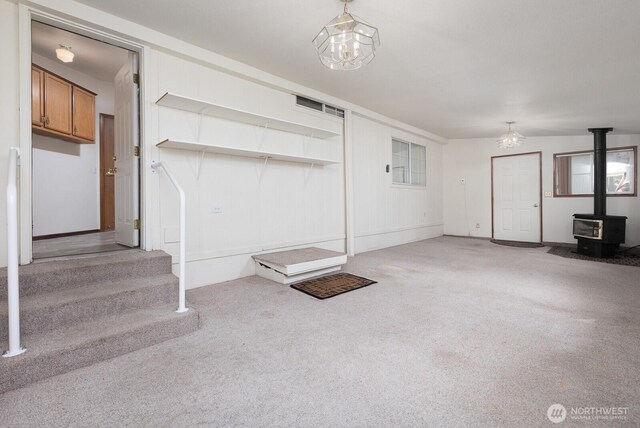unfurnished living room with a wood stove, carpet flooring, and stairs