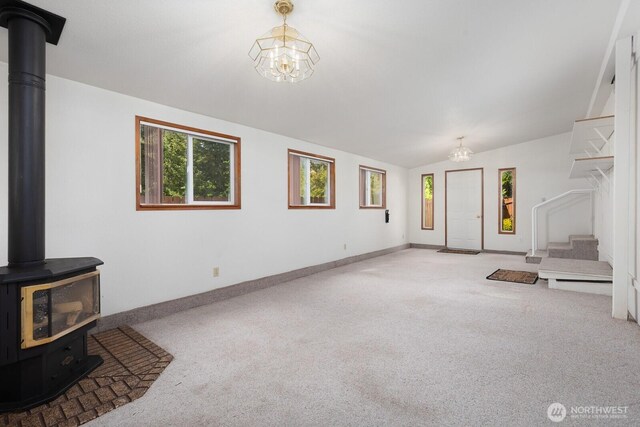 unfurnished living room with a healthy amount of sunlight, carpet, a wood stove, and a chandelier