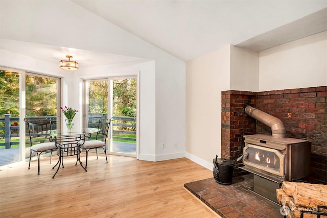 living area with a wood stove, vaulted ceiling, wood finished floors, and plenty of natural light