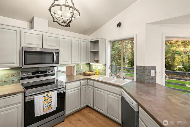 kitchen with a chandelier, stainless steel appliances, open shelves, vaulted ceiling, and a sink