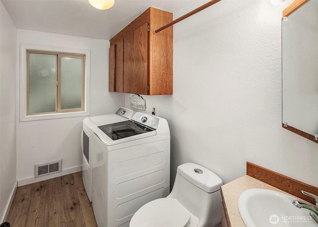 interior space featuring a sink, washing machine and dryer, visible vents, wood finished floors, and laundry area