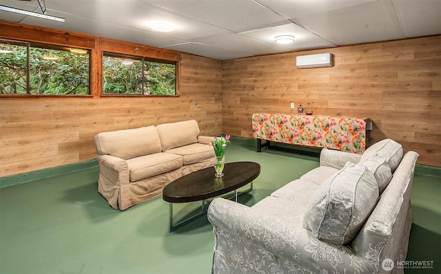 living area featuring concrete floors, wooden walls, a wall mounted air conditioner, and a drop ceiling