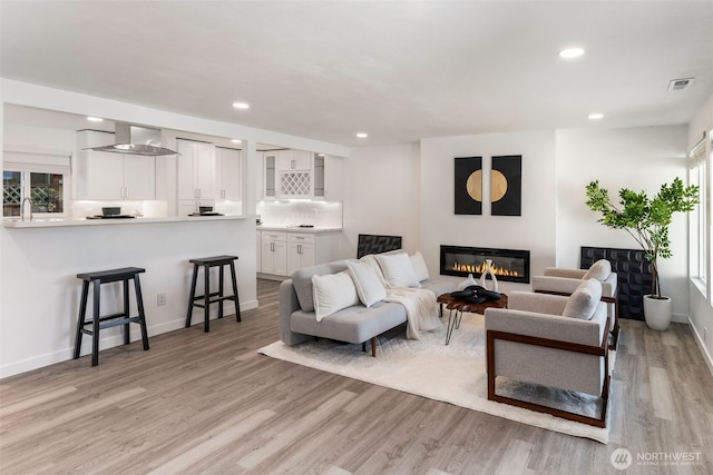 living area with recessed lighting, a glass covered fireplace, light wood-type flooring, visible vents, and plenty of natural light