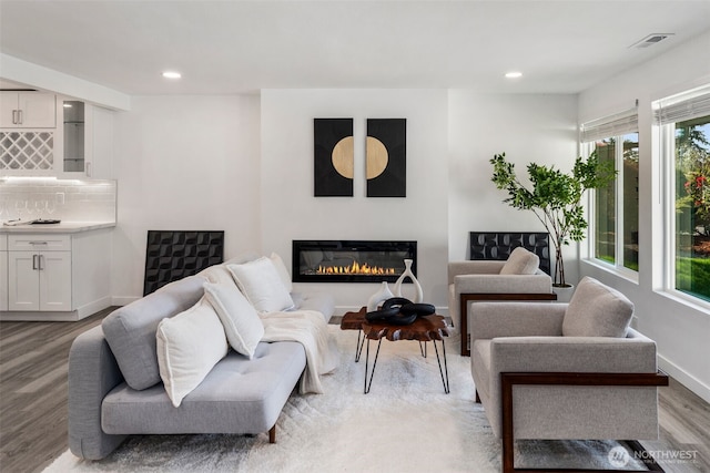 living room with light wood-type flooring, visible vents, a healthy amount of sunlight, and a glass covered fireplace
