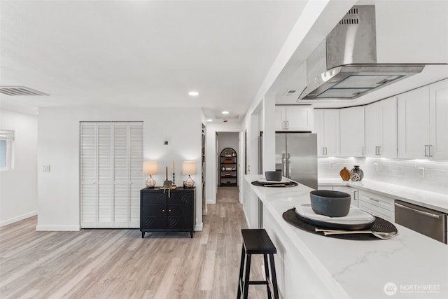 kitchen with wall chimney range hood, white cabinets, visible vents, stainless steel appliances, and light wood-style floors