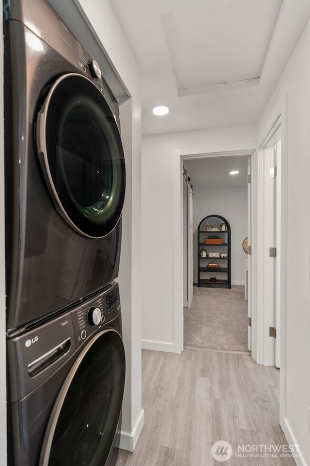 washroom featuring wood finished floors, stacked washer and clothes dryer, laundry area, and baseboards