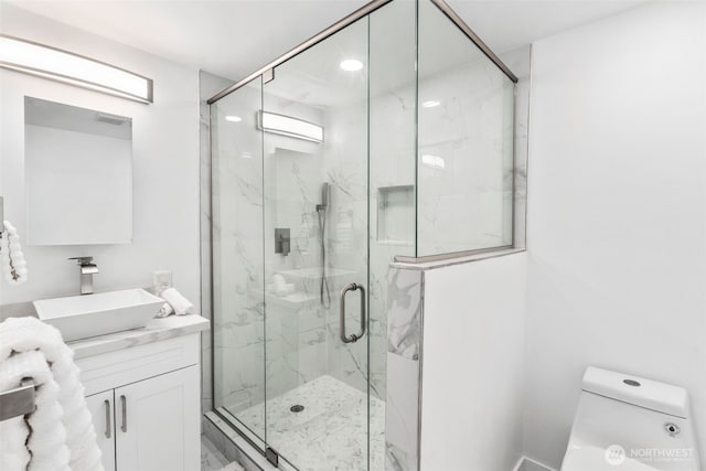 full bath with a marble finish shower, toilet, and vanity