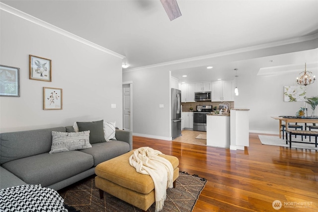 living area featuring baseboards, ornamental molding, light wood-style flooring, and a notable chandelier
