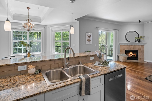 kitchen featuring a tiled fireplace, wood finished floors, dishwasher, a sink, and ornamental molding
