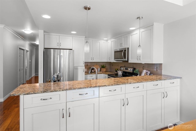 kitchen with light stone counters, a peninsula, white cabinets, and stainless steel appliances