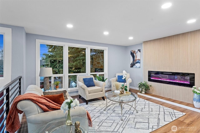living area featuring a glass covered fireplace, wood finished floors, and recessed lighting