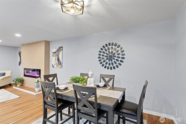 dining room with baseboards, recessed lighting, wood finished floors, and a large fireplace