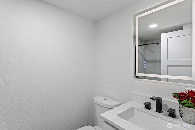 bathroom with toilet, a textured wall, walk in shower, and vanity