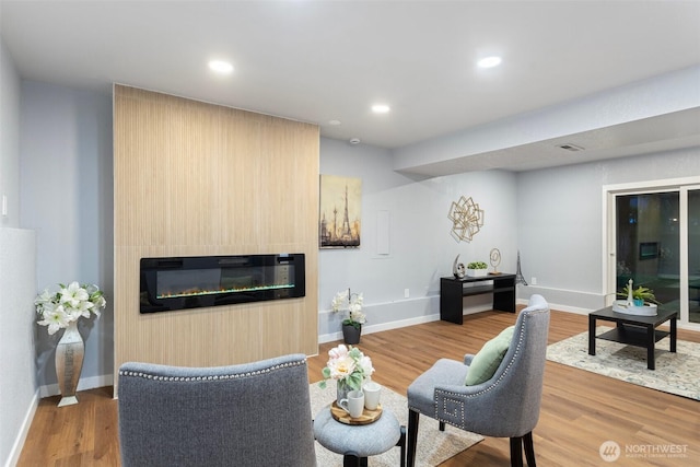 living area with baseboards, recessed lighting, wood finished floors, and a glass covered fireplace