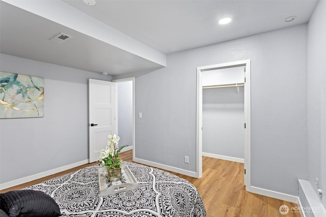 bedroom with a walk in closet, light wood-style flooring, and baseboards