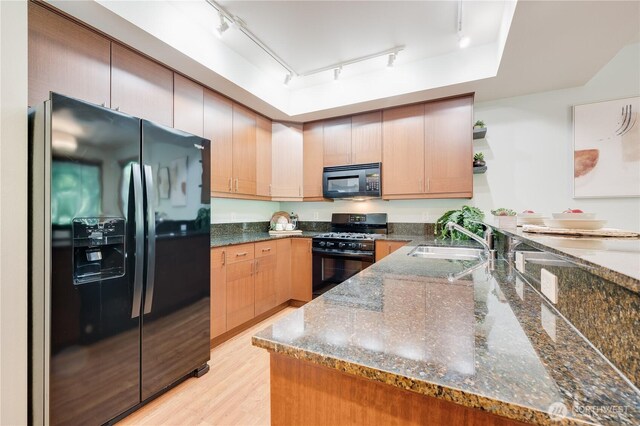 kitchen featuring black appliances, a sink, track lighting, open shelves, and dark stone countertops