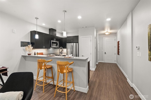 kitchen with stainless steel appliances, dark cabinetry, dark wood-style floors, a peninsula, and a sink