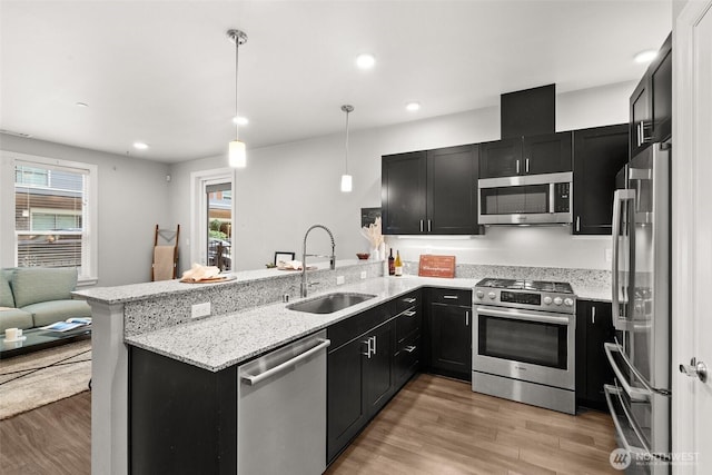 kitchen featuring a sink, appliances with stainless steel finishes, a peninsula, light wood-style flooring, and recessed lighting