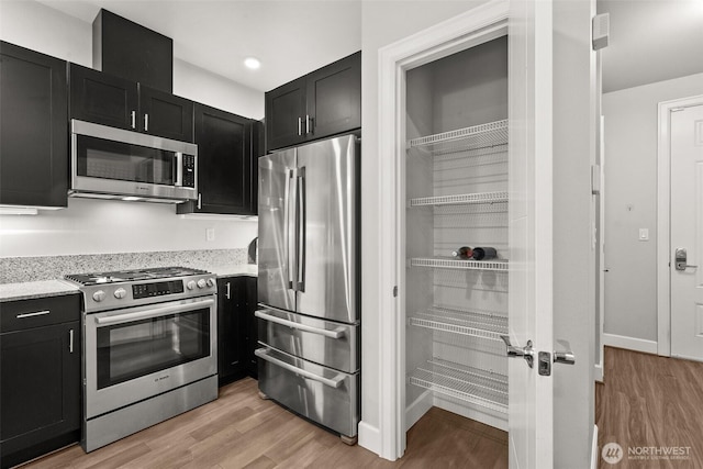 kitchen with appliances with stainless steel finishes, dark cabinetry, light stone counters, and light wood finished floors