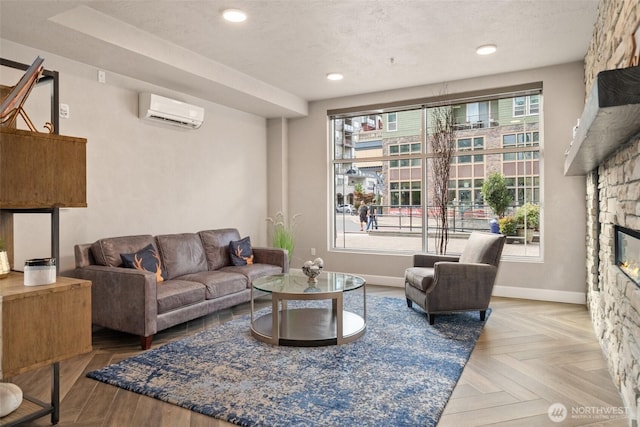 living room with a wall unit AC, a stone fireplace, baseboards, and recessed lighting