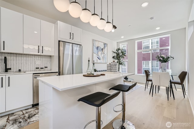 kitchen with a sink, stainless steel appliances, tasteful backsplash, a breakfast bar area, and light countertops