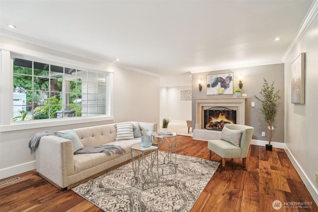 living area with crown molding, visible vents, wood finished floors, and a warm lit fireplace