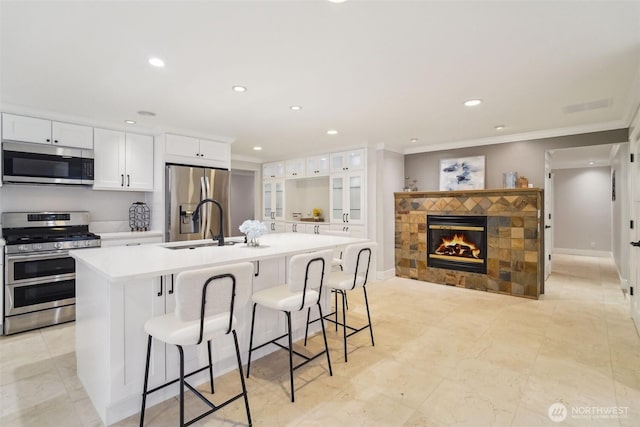 kitchen with an island with sink, stainless steel appliances, recessed lighting, and ornamental molding