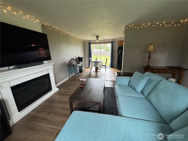 living room with a textured ceiling, baseboards, a glass covered fireplace, wood finished floors, and a ceiling fan
