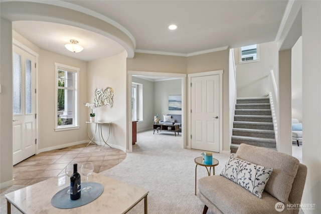 carpeted foyer with crown molding, baseboards, stairs, and arched walkways