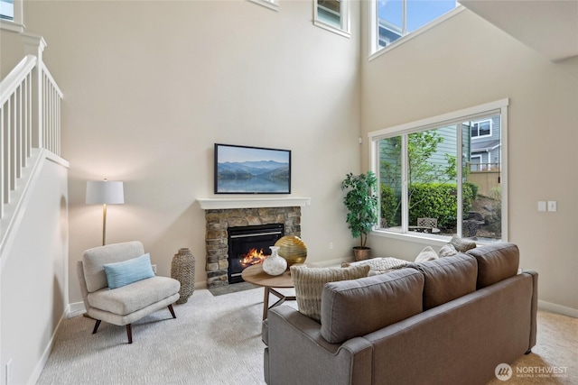 living room featuring a high ceiling, a stone fireplace, baseboards, and carpet
