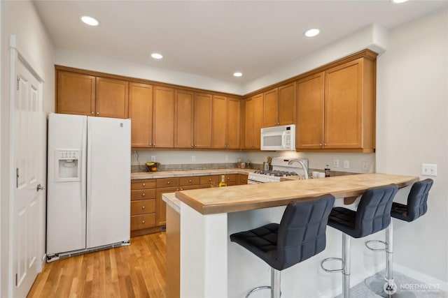 kitchen featuring brown cabinetry, light countertops, a peninsula, and white appliances
