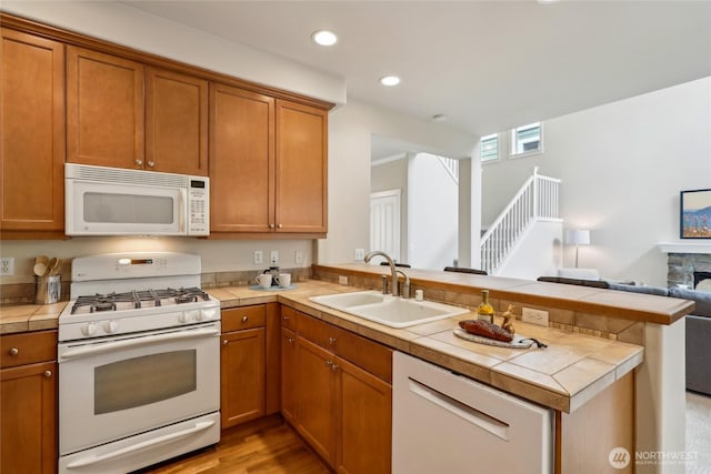 kitchen with a sink, white appliances, a peninsula, open floor plan, and tile countertops