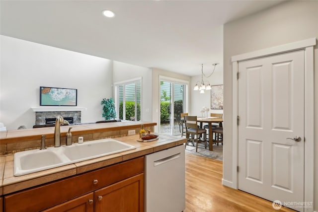 kitchen featuring brown cabinetry, a fireplace, dishwashing machine, a sink, and light wood finished floors