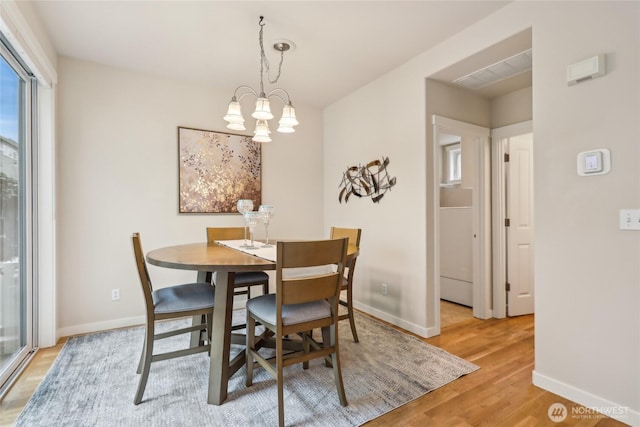 dining space featuring baseboards, light wood-type flooring, and a notable chandelier