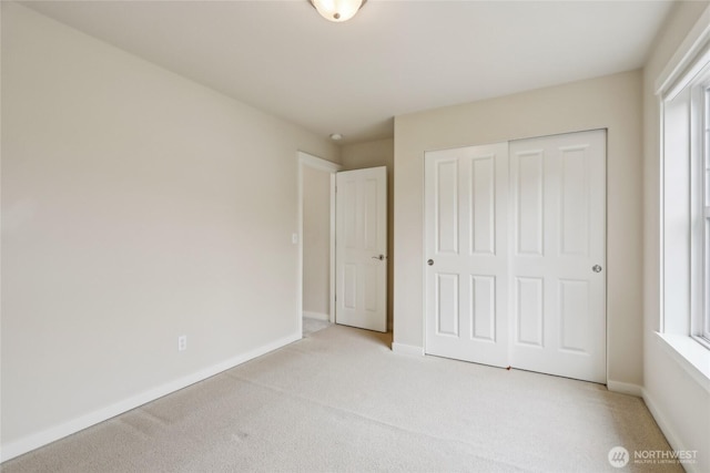 unfurnished bedroom featuring baseboards, light colored carpet, and a closet