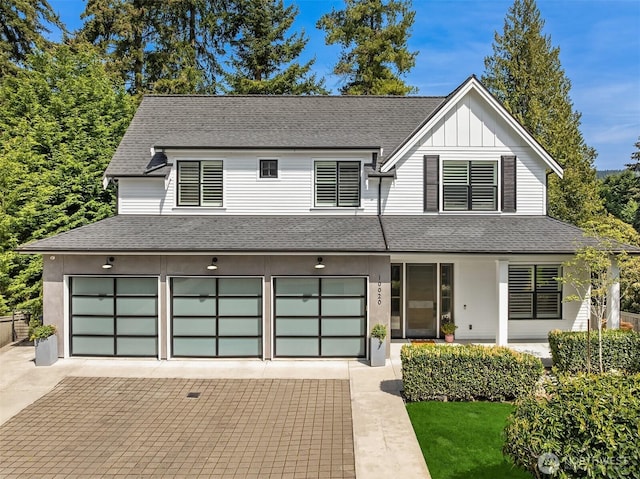 view of front of property featuring decorative driveway, a shingled roof, an attached garage, and board and batten siding