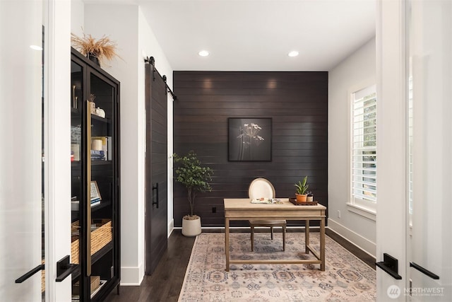 office space with a barn door, wood finished floors, baseboards, an accent wall, and recessed lighting