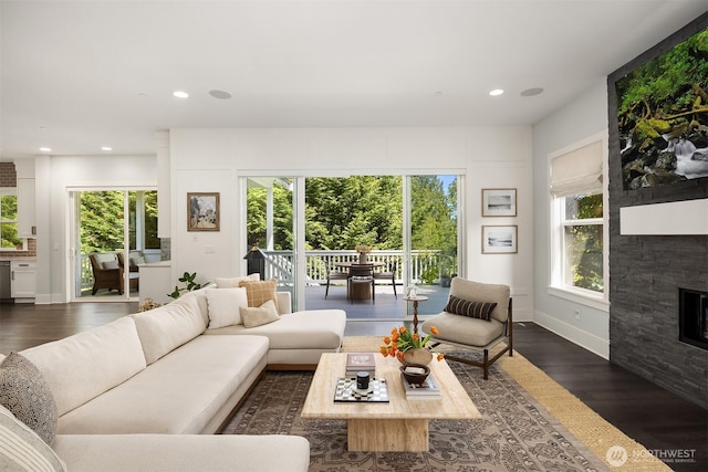 living area featuring dark wood-type flooring, recessed lighting, plenty of natural light, and a stone fireplace