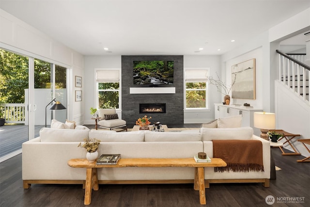 living area with a healthy amount of sunlight, a large fireplace, stairs, and wood finished floors