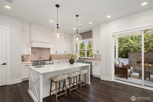 kitchen featuring dark wood-style flooring, a center island with sink, white cabinetry, tasteful backsplash, and a sink