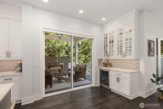 bar with backsplash, dark wood-style flooring, a glass covered fireplace, wine cooler, and recessed lighting