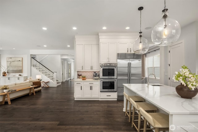 kitchen with backsplash, appliances with stainless steel finishes, a sink, white cabinets, and recessed lighting