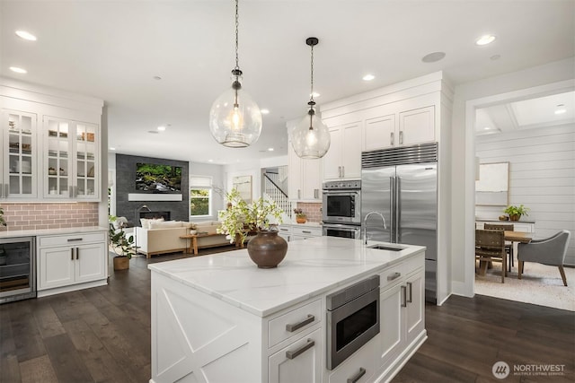 kitchen with built in appliances, backsplash, white cabinets, and wine cooler