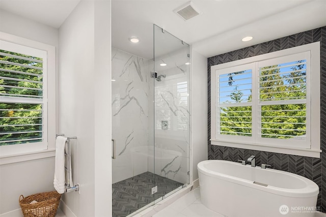 bathroom with a freestanding bath, a marble finish shower, recessed lighting, tile walls, and visible vents