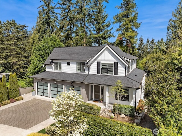 view of front of home with an attached garage, decorative driveway, board and batten siding, and a shingled roof