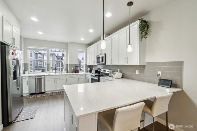 kitchen featuring decorative backsplash, appliances with stainless steel finishes, a sink, a peninsula, and white cabinetry