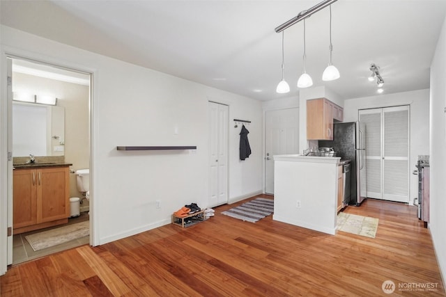 kitchen with a sink, backsplash, light wood-style flooring, baseboards, and hanging light fixtures