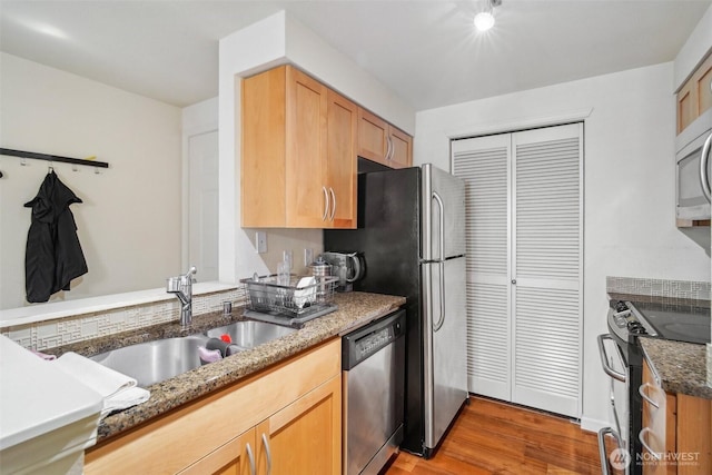 kitchen with stone countertops, stainless steel appliances, light wood-style floors, and a sink
