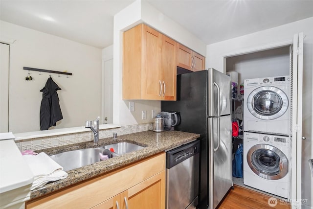 kitchen featuring a sink, light brown cabinets, stacked washer and clothes dryer, light stone counters, and stainless steel dishwasher